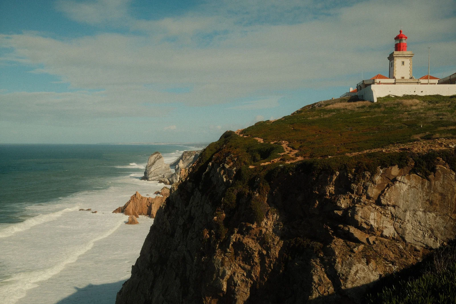 Phare côtier blanc à toit rouge dominant l'océan et une plage, vue proche du panorama offert par la webcam du phare de Chassiron